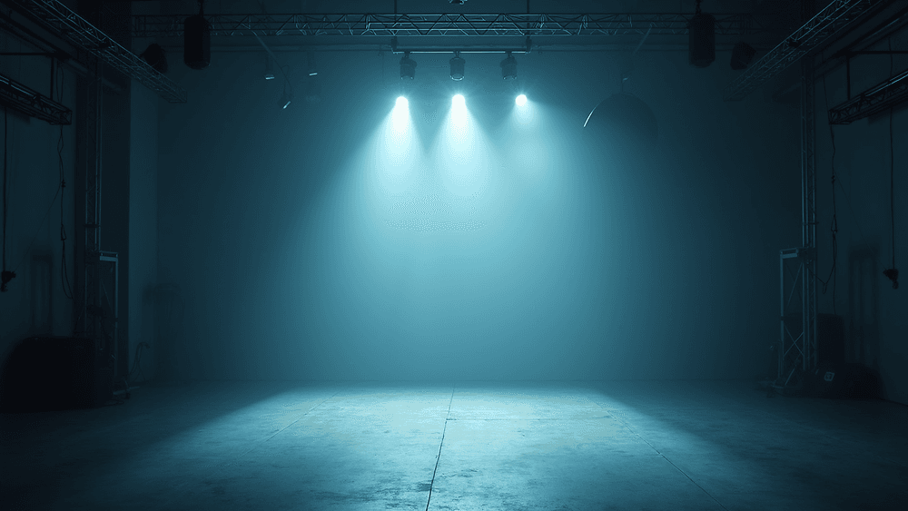 Sala de eventos vacía y en penumbra, con truss en el techo y tres focos atravesando la niebla